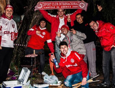 Grupo de torcedores do Internacional com camisas e casacos vermelhos exibindo um cachecol do clube à noite, nos arredores do Estádio Beira-Rio, antes de jogo da Libertadores de 2015