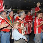 Torcedores do Internacional com camisas e bandeiras vermelhas cantam acompanhados por um acordeão em saguão de aeroporto, à espera dos campeões mundiais, em janeiro de 2007