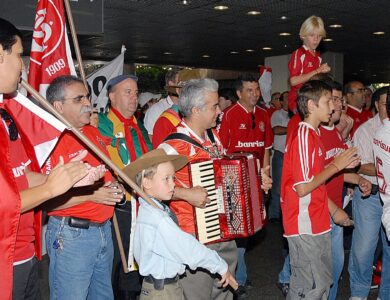 Torcedores do Internacional com camisas e bandeiras vermelhas cantam acompanhados por um acordeão em saguão de aeroporto, à espera dos campeões mundiais, em janeiro de 2007