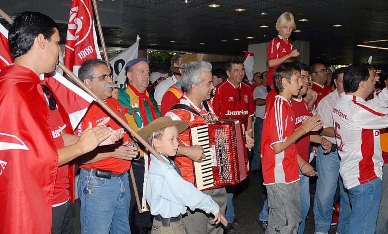 Torcedores do Internacional com camisas e bandeiras vermelhas cantam acompanhados por um acordeão em saguão de aeroporto, à espera dos campeões mundiais, em janeiro de 2007