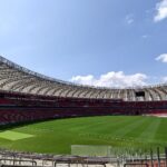 Vista interna do Estádio Beira-Rio vazio em 2024, com gramado, cadeiras vermelhas e a cobertura circular aberta para o céu azul